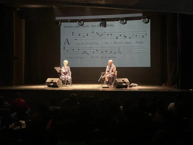 Due musicisti sul palco con uno spartito proiettato alle spalle